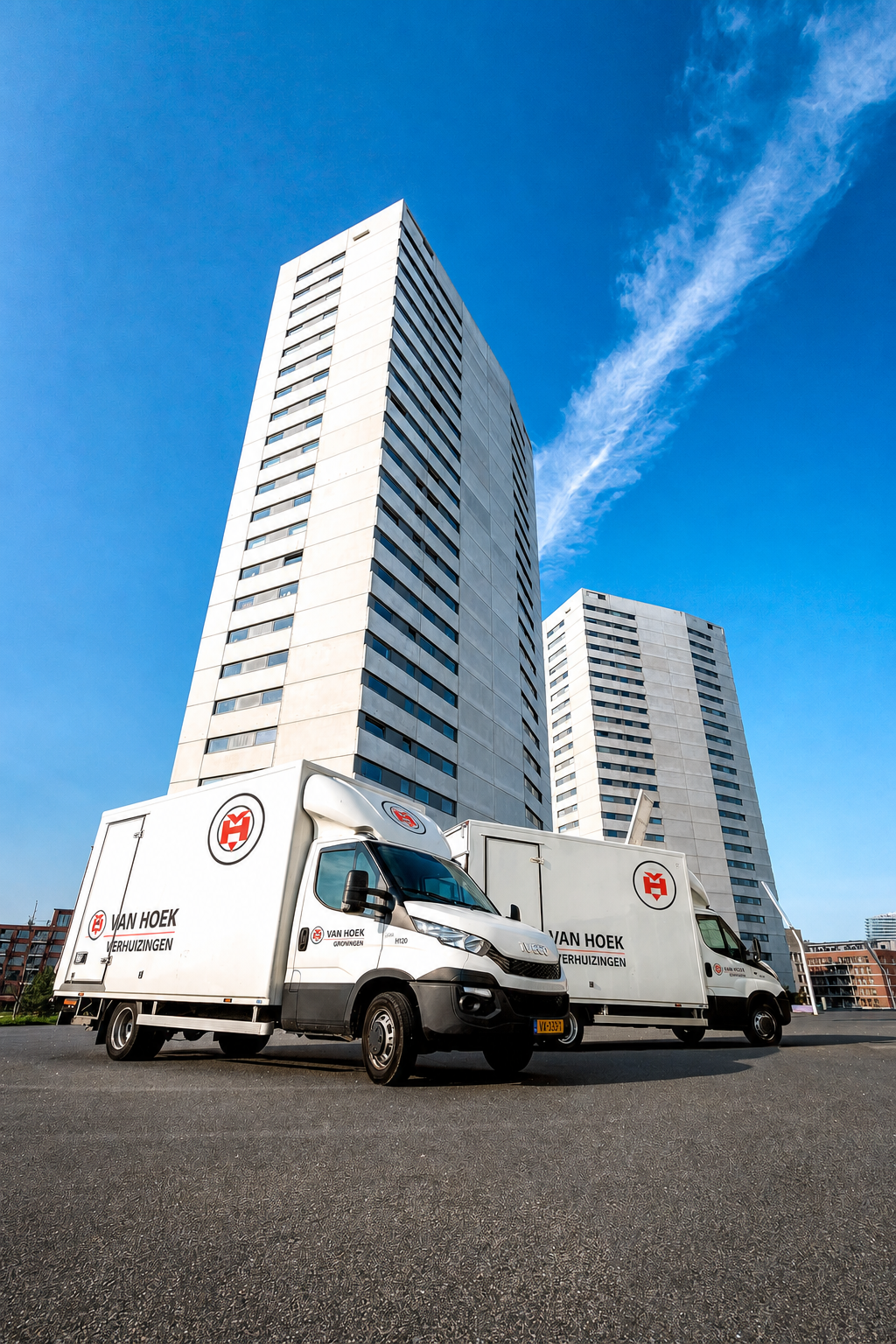 Twee wagens van Van Hoek Verhuizingen voor twee grote witte flats in kikkerperspectief.